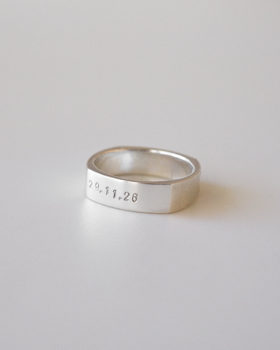 Silver ring with engraved date on a light gray background