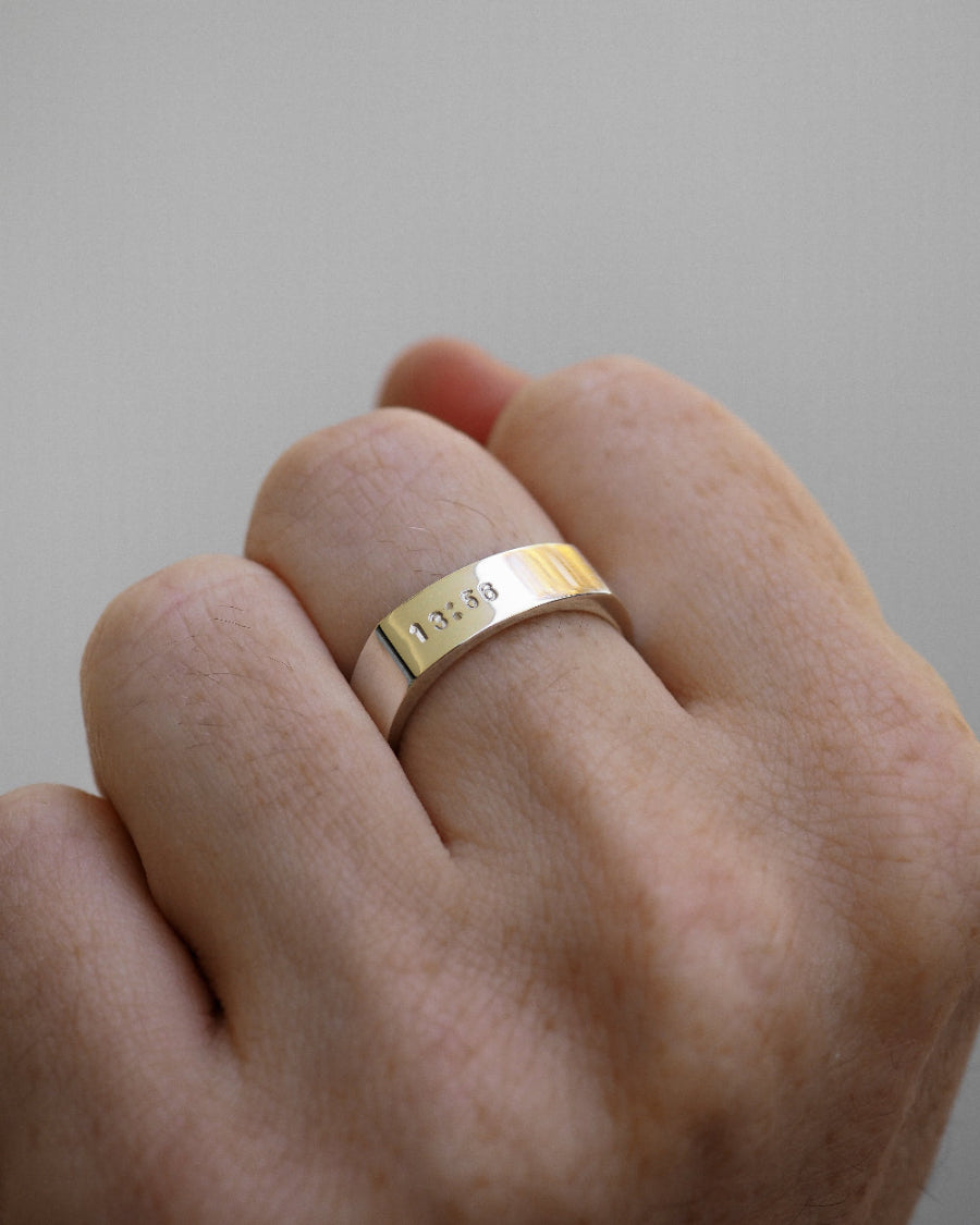 Gold ring with engraved text on a person's finger against a neutral background