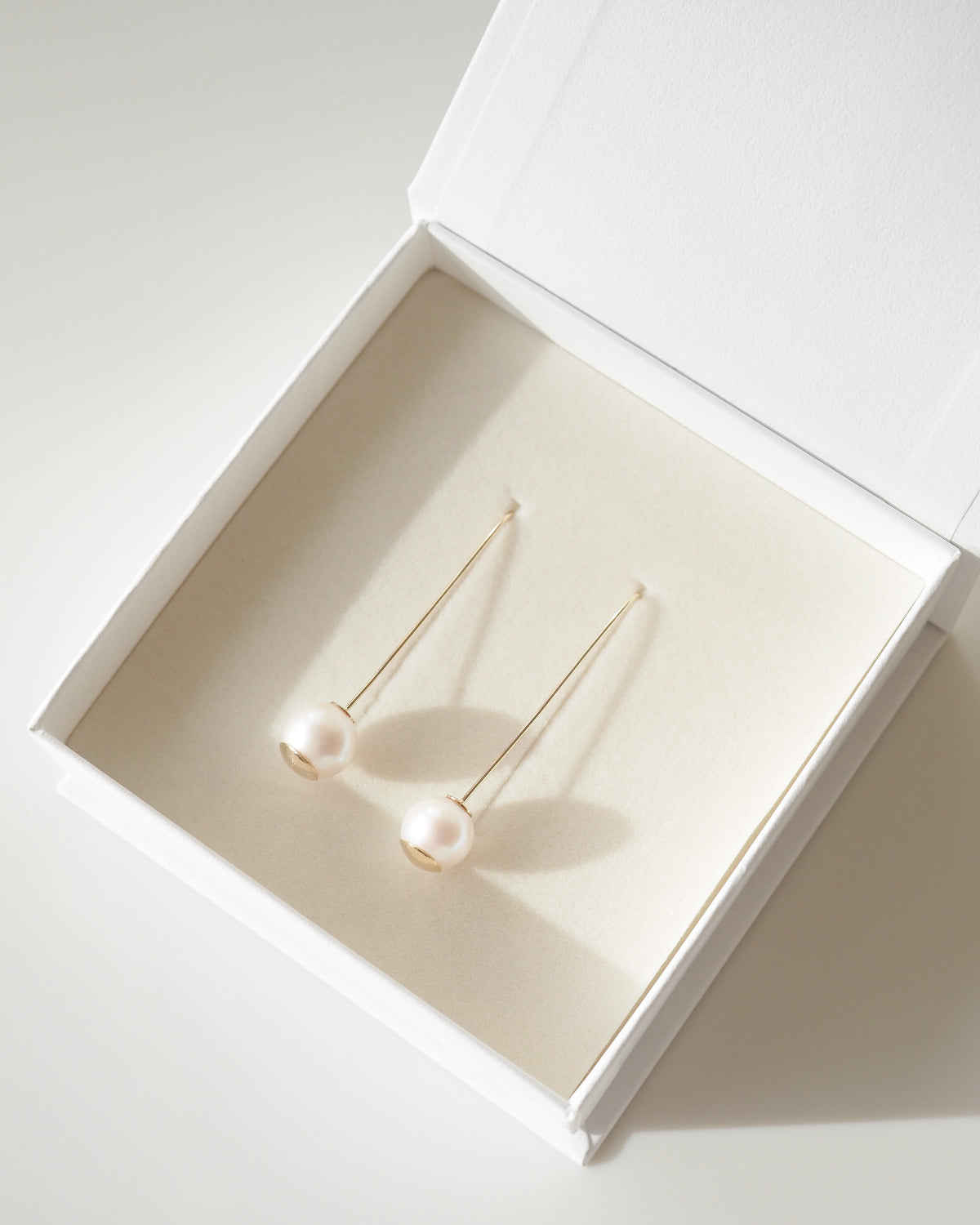 Gold earrings with pearls in a white jewelry box on a light background