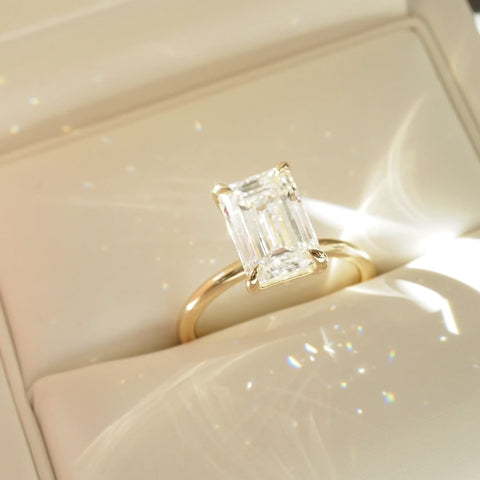 Emerald cut diamond ring with a gold band in a cream box. Luxurious, elegant jewellery design.