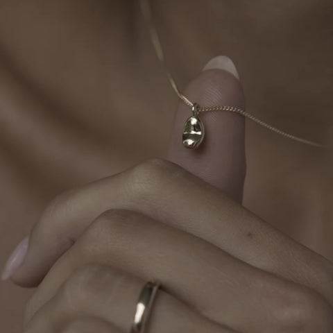 Close detail of the Baby in Time bean pendant, sized to a 7-8 week embryo