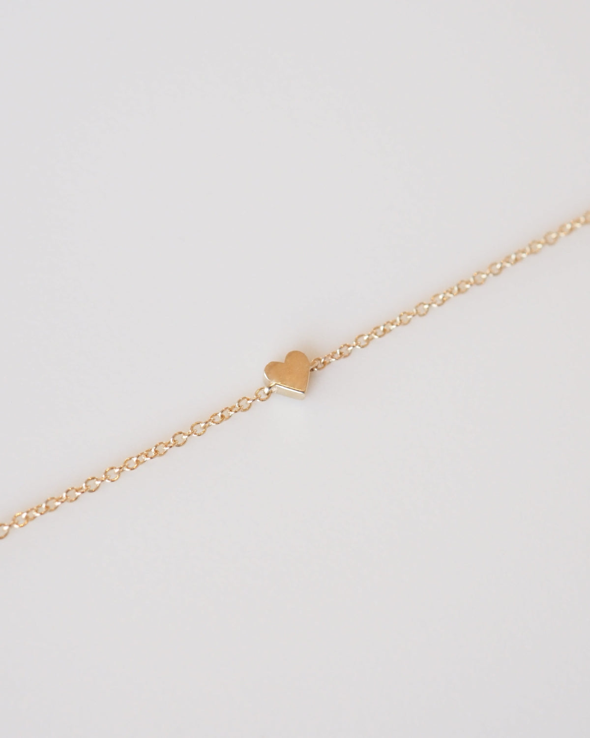 Gold bracelet with a heart charm on a light gray background