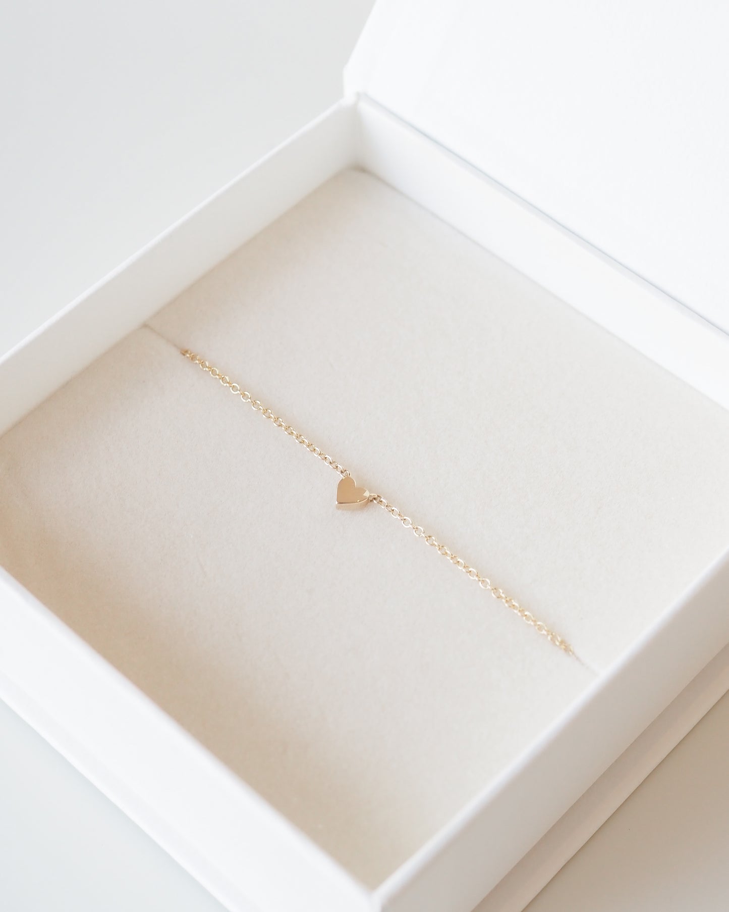 Gold necklace with a heart pendant in an open jewelry box on a white background